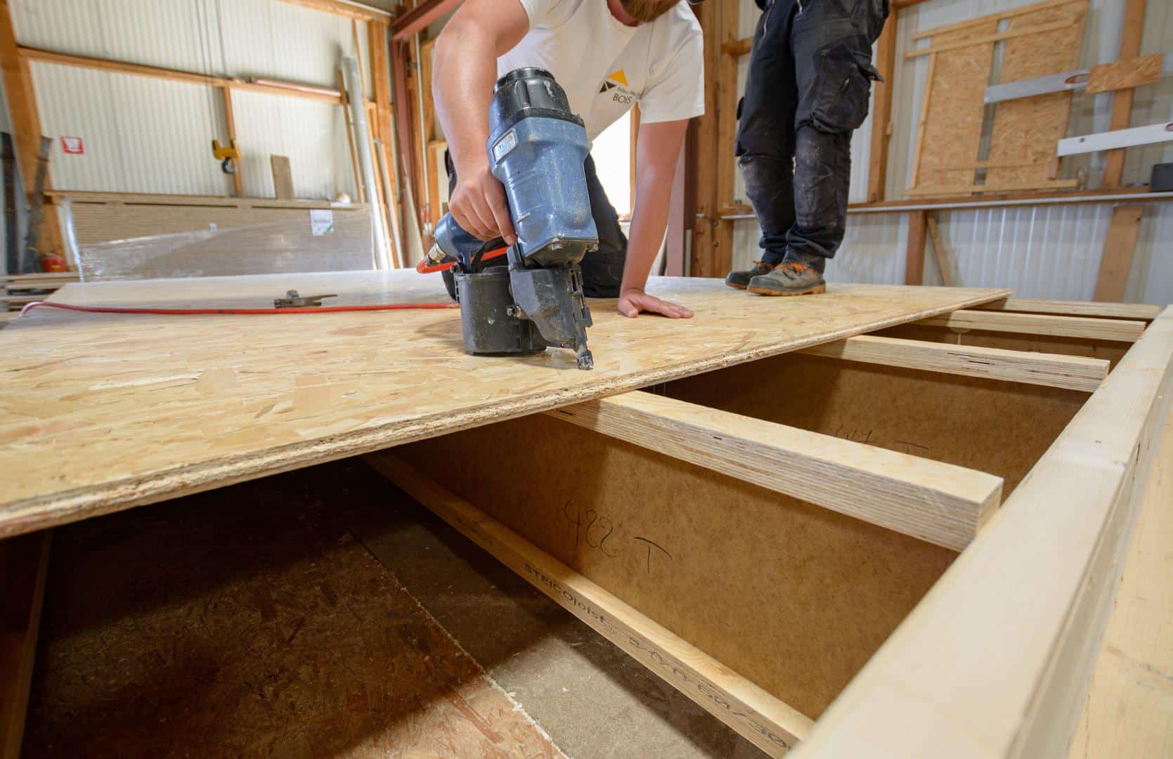 Ouvrier de Natur’Element Bois clouant une planche de bois sur une structure.