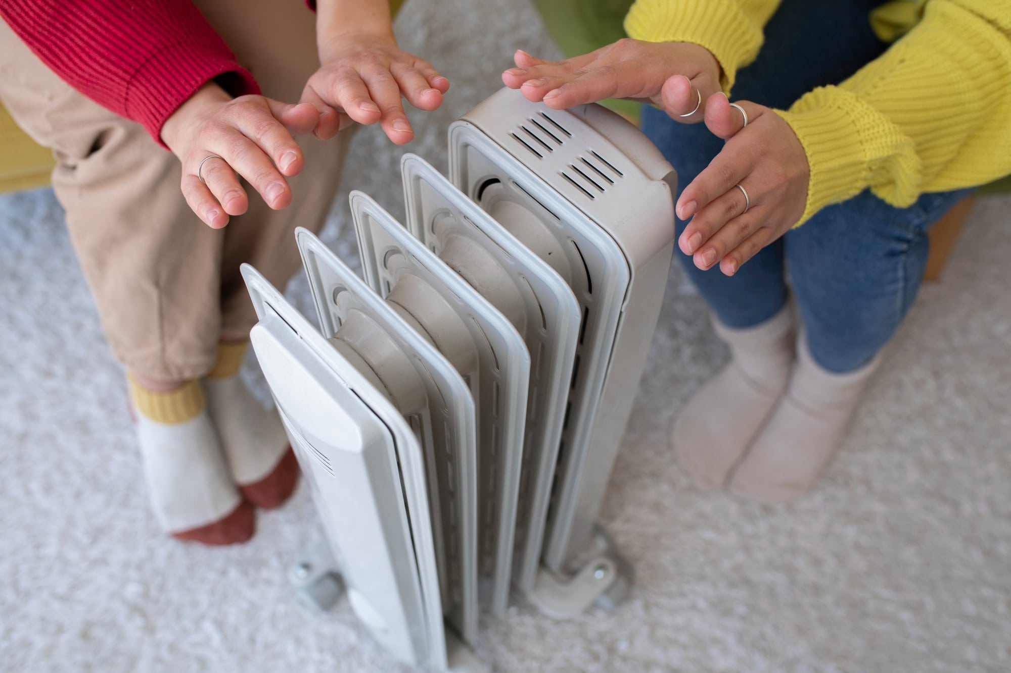 Personnes assises autour d’un radiateur dans un intérieur chauffé.